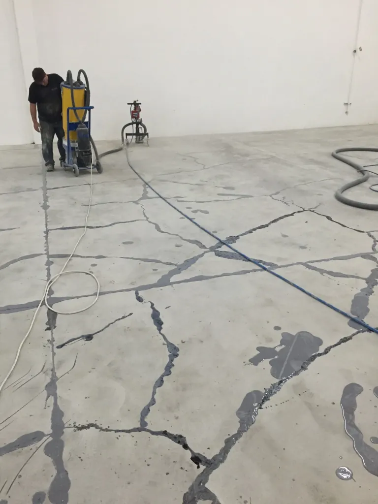 Large concrete floor with many cracks filled with grey repair material