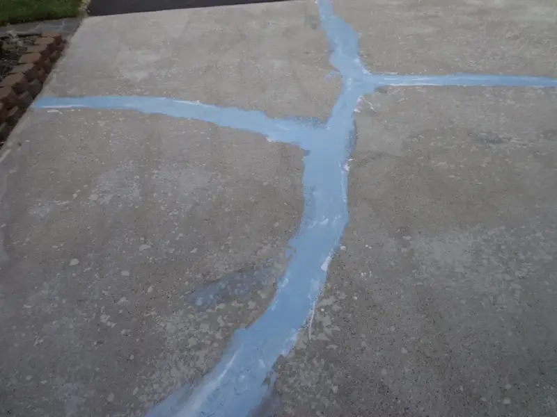 Concrete driveway with long cracks filled with blue-grey repair material