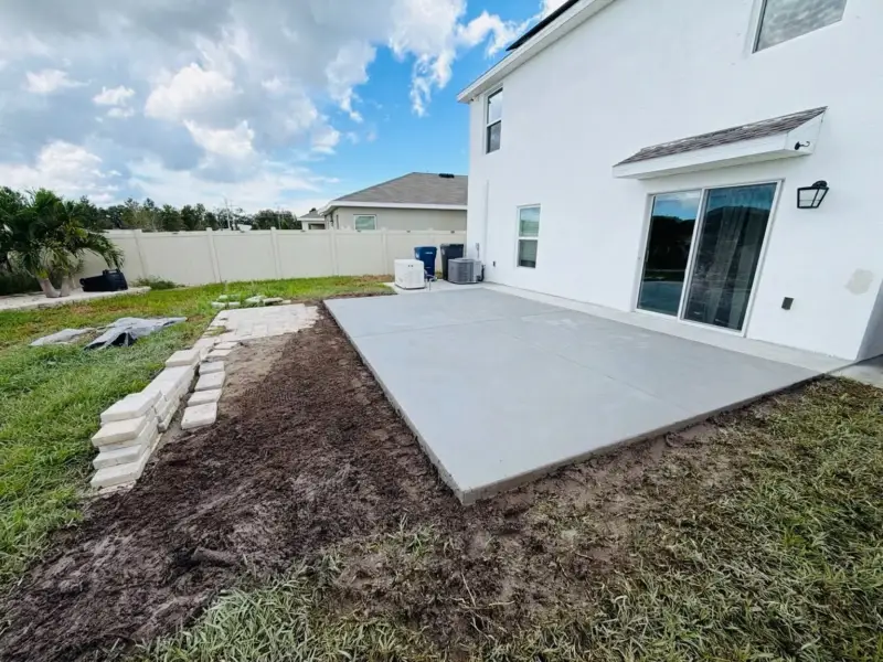 New concrete patio slab poured behind a white two-story home