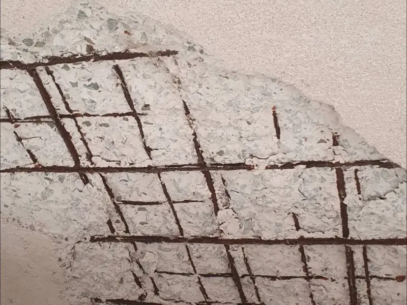 Concrete surface broken away to show a grid of rusted reinforcing steel