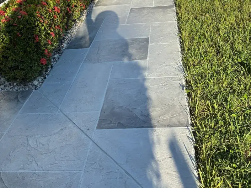 Concrete walkway resurfaced with a grey slate-pattern overlay beside a hedge